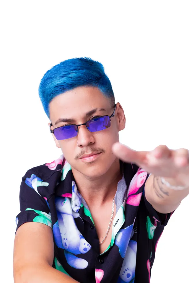 Patrick Richard de cabelo azul e óculos roxos, camisa estampada, estendendo a mão para a câmera